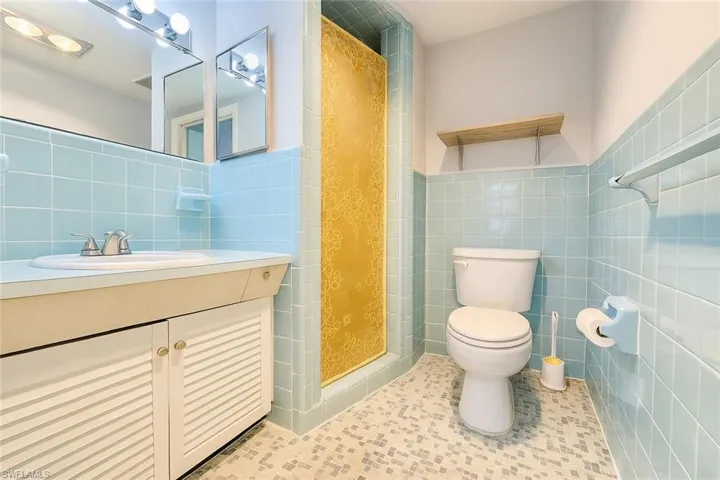Bathroom featuring a shower stall, vanity, tile walls, tile patterned floors, and wainscoting