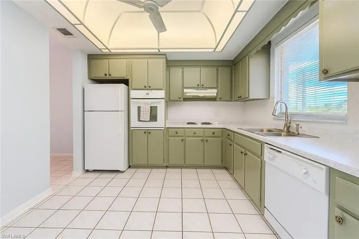 Kitchen with white appliances, light countertops, green cabinets, and light tile patterned flooring