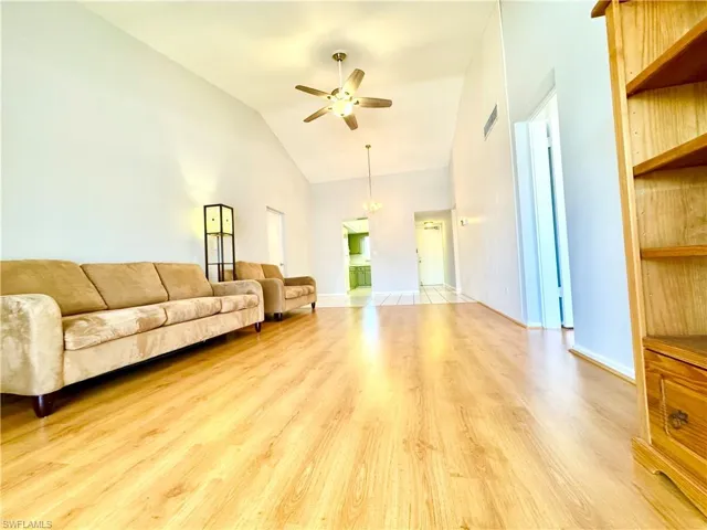 Living area with light wood-style floors, ceiling fan, and high vaulted ceiling