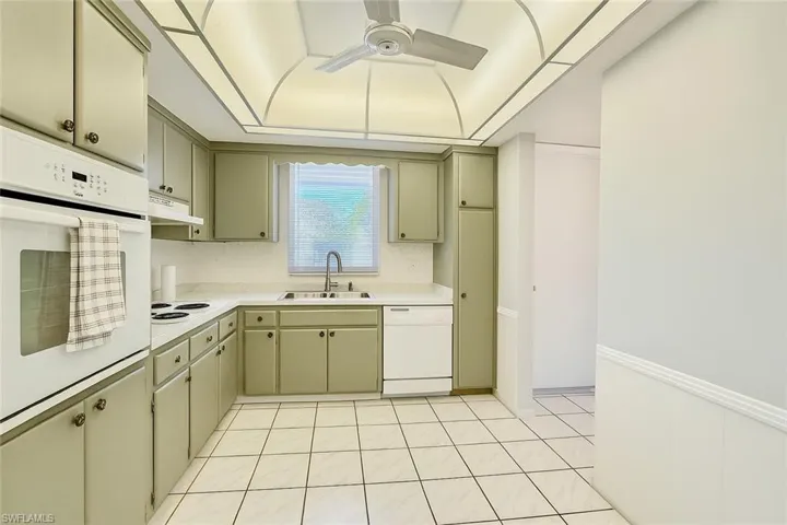 Kitchen featuring light countertops, white appliances, light tile patterned flooring, a ceiling fan, and under cabinet range hood