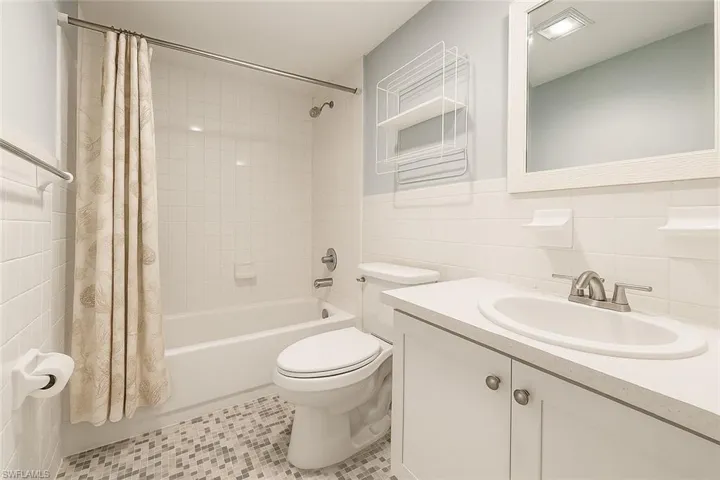 Full bath featuring tile walls, shower / bath combination with curtain, vanity, and light tile patterned floors