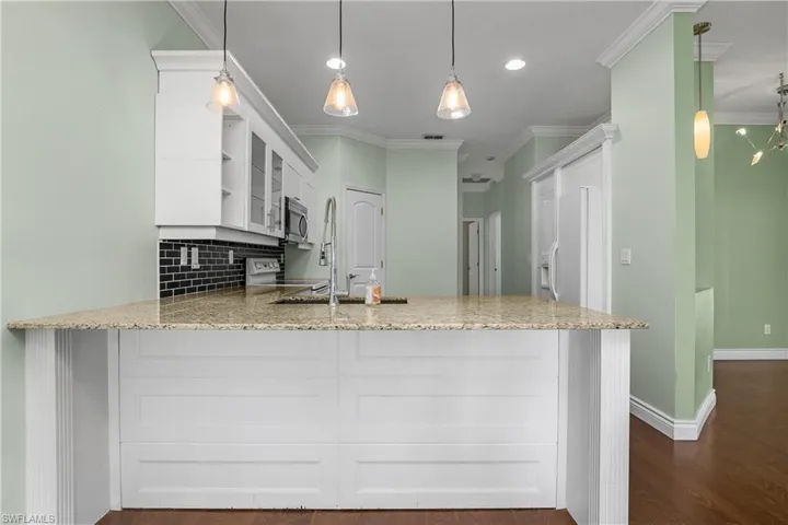 Kitchen featuring light stone countertops, a breakfast bar,white cabinetry, pendant lighting, and ornamental molding