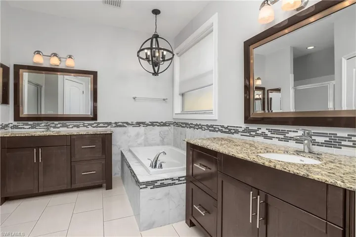 Primary Bathroom with a garden tub, two vanities, hanging lights, and light tile patterned floors