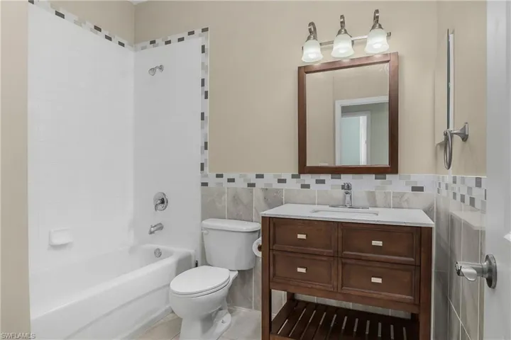 Second Bathroom featuring vanity, washtub / shower combination, decorative tile walls, tile patterned flooring, and wainscoting