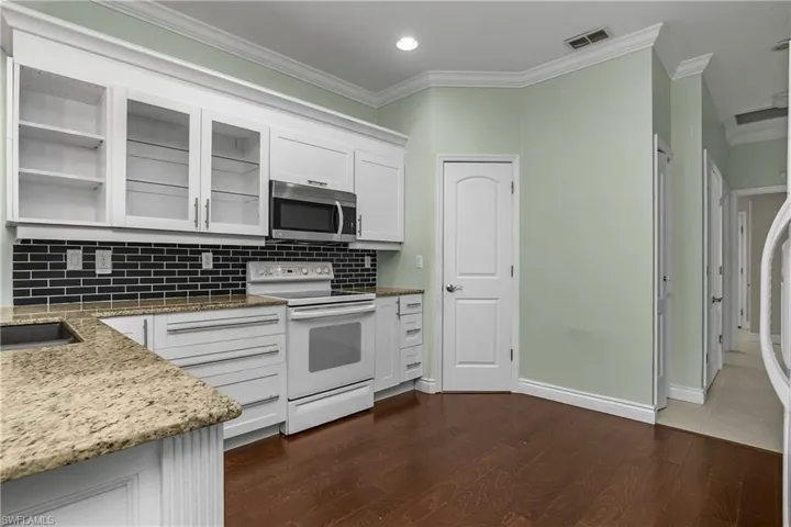 Kitchen with white electric range, light stone counters, white cabinets, stainless steel microwave, and crown molding