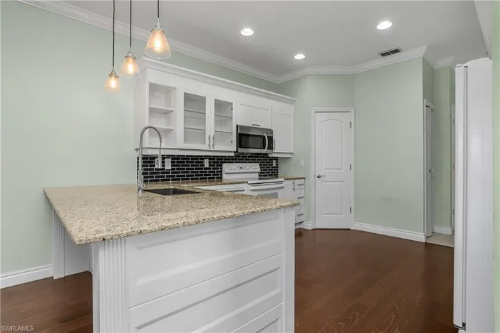 Kitchen with white cabinetry, white appliances, ornamental molding, glass insert cabinets