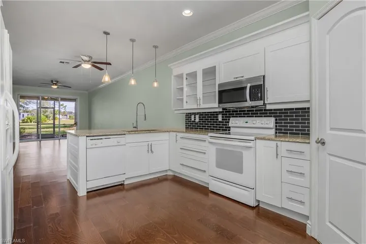 Kitchen with white appliances, crown molding, white cabinets, light stone counters, and pendant lighting