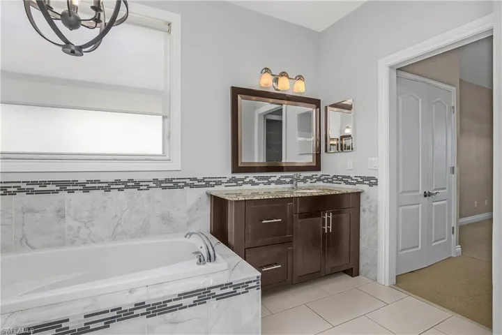 Primary bath featuring a bath, light tile patterned floors, vanity, decorative tile walls, and a chandelier