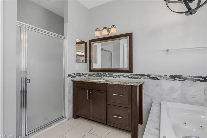 Primary bath featuring a bath, light tile patterned floors, vanity, walk in shower, decorative tile walls, and a chandelier