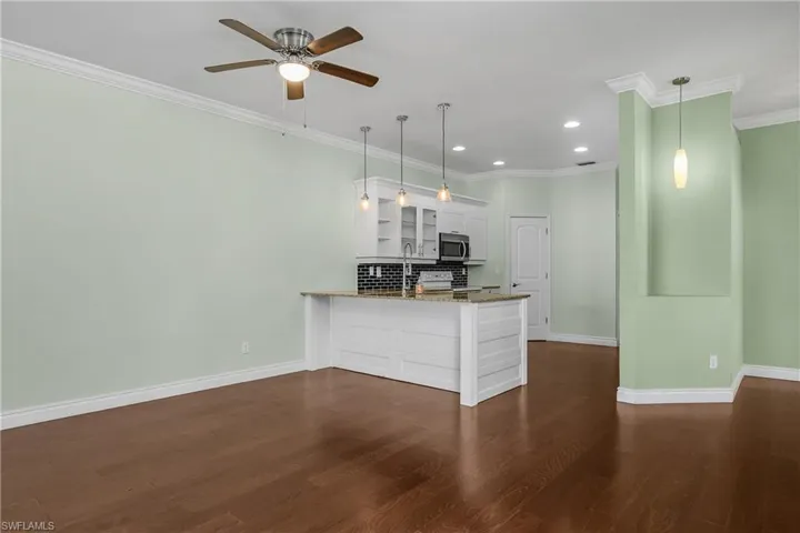 Kitchen with white cabinetry, light stone countertops, pendant lighting, a breakfast bar, and crown molding