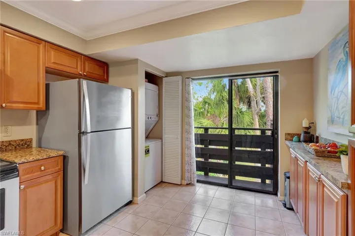 Kitchen featuring stainless steel fridge, granite countertops, light tile floors, and stacked washer and  dryer