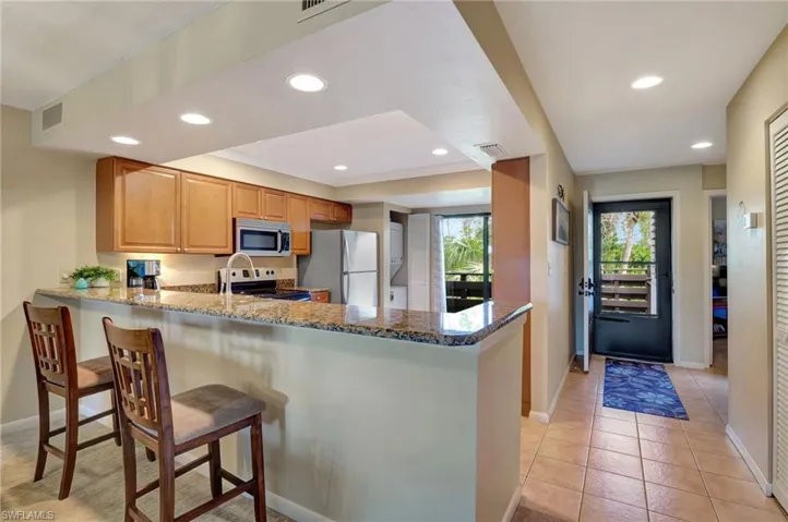 Kitchen featuring kitchen peninsula, appliances with stainless steel finishes, light tile floors, granite countertops, and a breakfast bar area