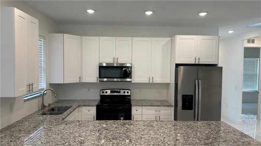 Kitchen with healthy amount of natural light, light stone countertops, stainless steel appliances, white cabinets, and recessed lighting