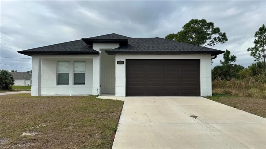 View of front of home featuring a shingled roof, driveway, a garage, a front lawn, and stucco siding