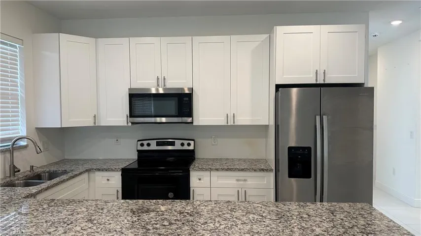 Kitchen featuring stainless steel appliances, light stone counters, and white cabinetry