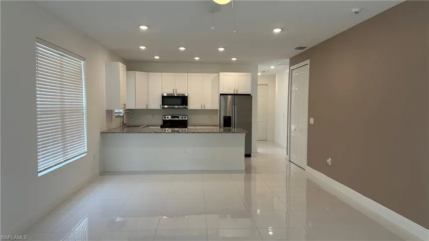Kitchen with dark stone counters, white cabinets, a peninsula, stainless steel appliances, and recessed lighting