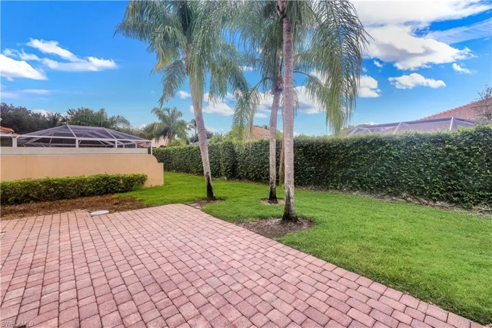 Expansive outdoor space featuring a paver patio, lush green lawn, mature palm trees, and a privacy hedge