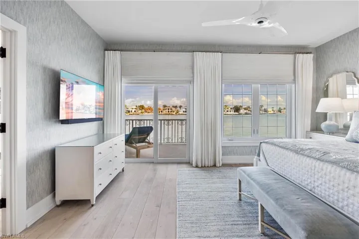 Primary bedroom featuring views of bay, engineered wood flooring, grasscloth wallpaper, window treatments, and access to balcony over bay