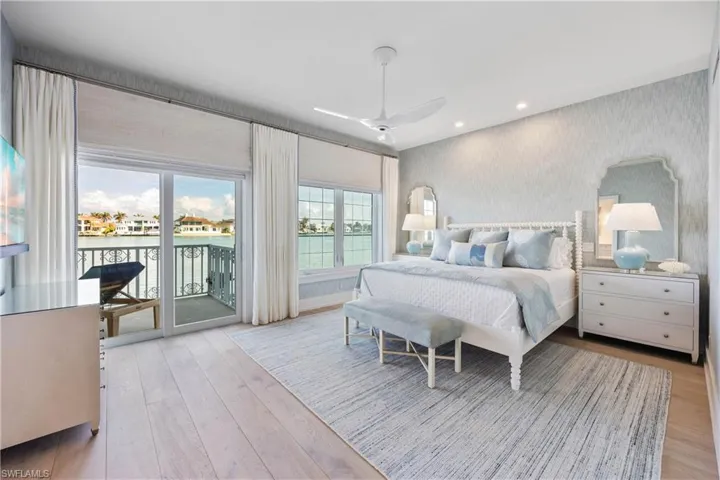 Primary bedroom featuring views of bay, engineered wood flooring, window treatments, grasscloth wallpaper, and access to balcony over bay