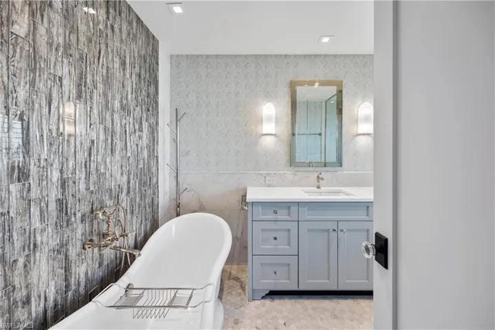 Primary suite bath featuring vanity, freestanding soakingtub, and waterfall tile design