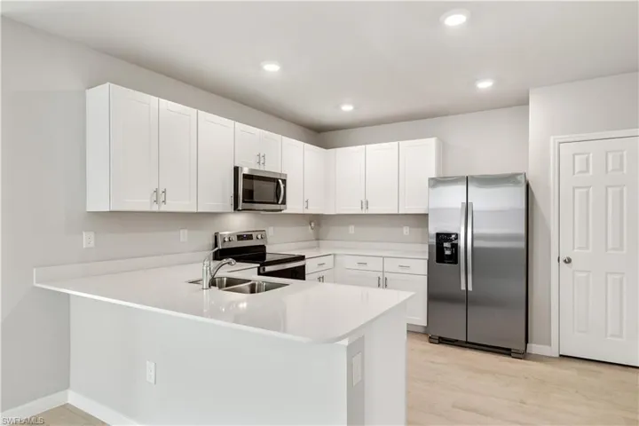 Kitchen featuring stainless steel appliances, white cabinets, light wood-type flooring, and kitchen peninsula