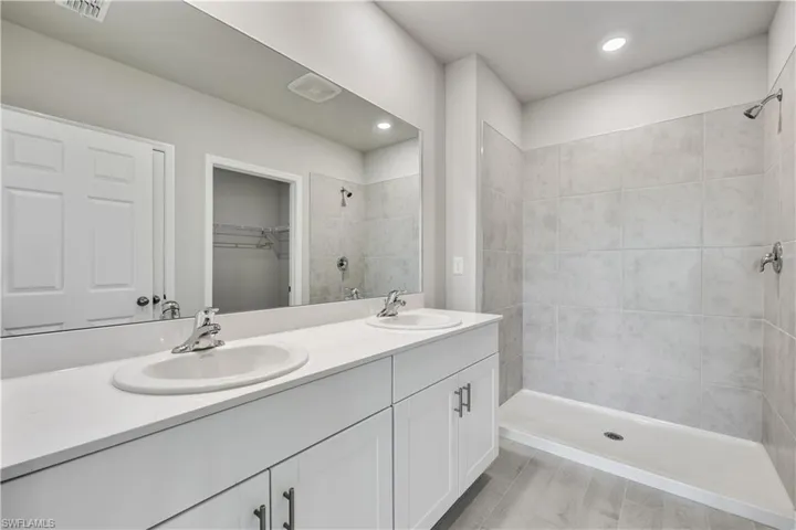 Bathroom with a tile shower, wood-type flooring, and dual bowl vanity