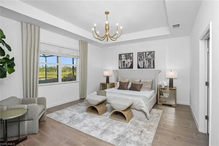 Bedroom with a raised ceiling, light wood finished floors, and a chandelier