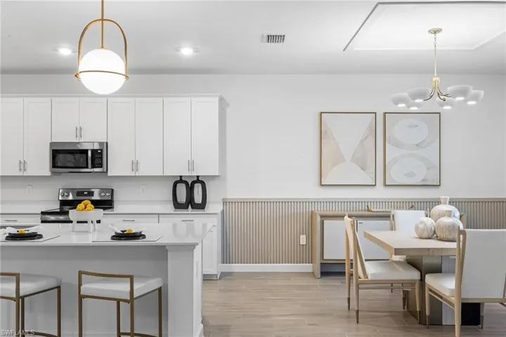 Kitchen featuring pendant lighting, a wainscoted wall, white cabinetry, stainless steel appliances, and a breakfast bar
