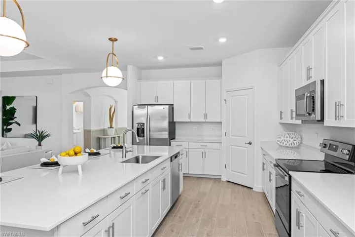 Kitchen featuring appliances with stainless steel finishes, white cabinetry, recessed lighting, light wood finished floors, and a center island with sink