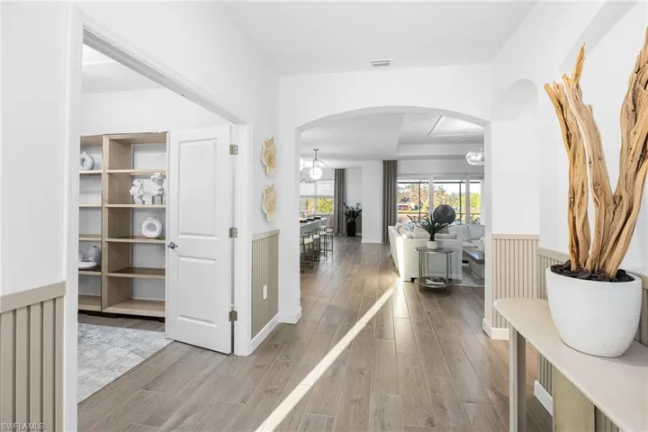 Hallway with arched walkways, light wood-style flooring, and a wainscoted wall
