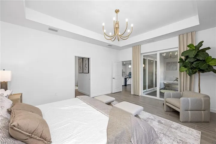 Bedroom with wood finished floors, a raised ceiling, and a chandelier