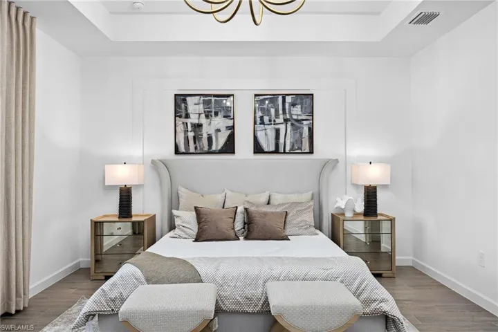 Bedroom with a raised ceiling, wood finished floors, and a chandelier