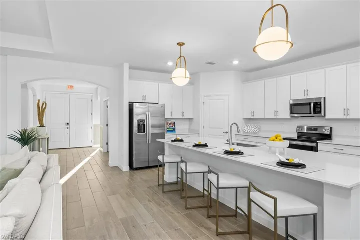 Kitchen with a kitchen breakfast bar, appliances with stainless steel finishes, arched walkways, white cabinets, and hanging light fixtures