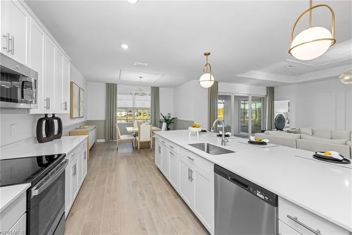 Kitchen with white cabinets, appliances with stainless steel finishes, hanging light fixtures, and open floor plan