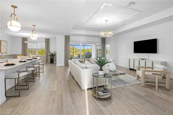 Living room featuring a tray ceiling, a chandelier, light wood-style floors, and plenty of natural light