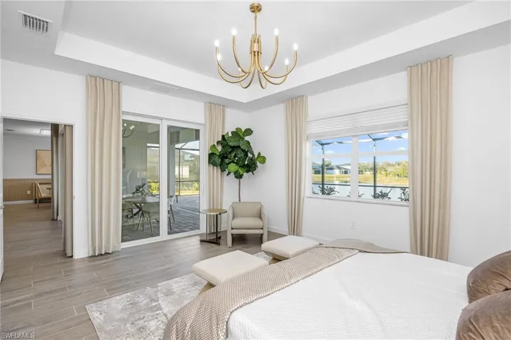 Bedroom featuring wood tiled floors, access to exterior, a water view, a tray ceiling, and a chandelier