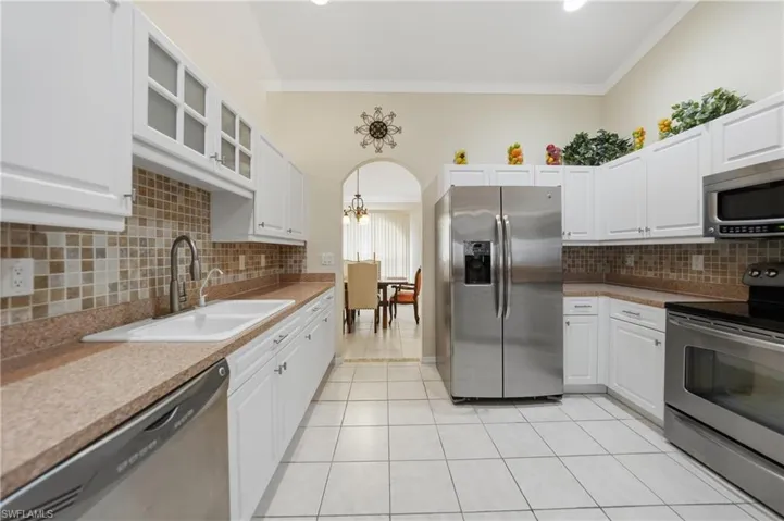 Kitchen with stainless steel appliances, glass insert cabinets, white cabinets, ornamental molding, and light tile patterned floors