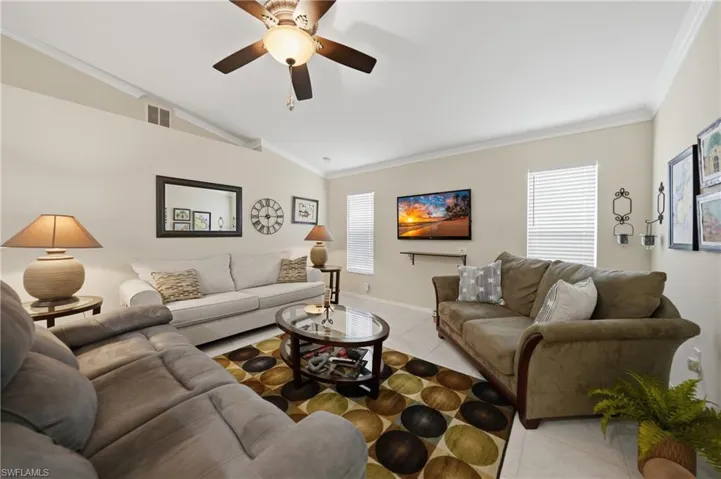 Living area featuring light tile patterned floors, ornamental molding, lofted ceiling, and ceiling fan