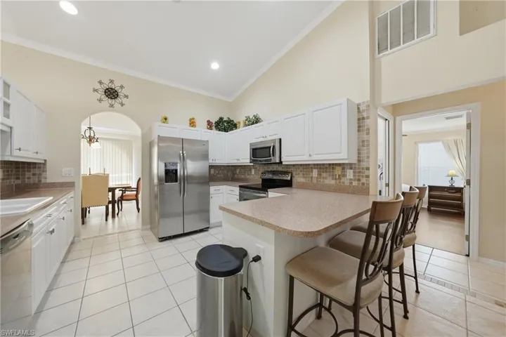 Kitchen featuring stainless steel appliances, white cabinets, light tile patterned flooring, a kitchen breakfast bar, and a peninsula