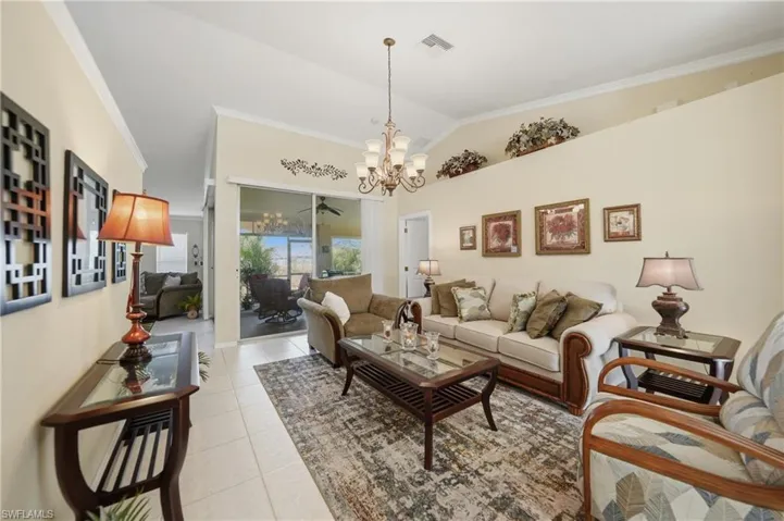 Living room with light tile patterned floors, ornamental molding, suspended lighting, and vaulted ceiling