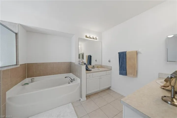 Bathroom featuring two vanities, a garden tub, and light tile patterned floors