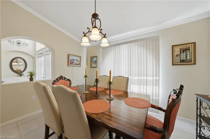 Dining space with a chandelier, light tile patterned flooring, ornamental molding, and arched walkways