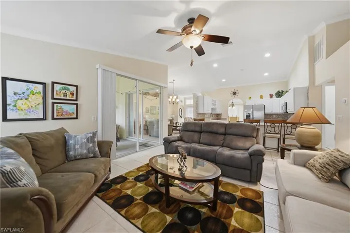 Living room with crown molding, light tile patterned floors, hanging lights, ceiling fan, and vaulted ceiling