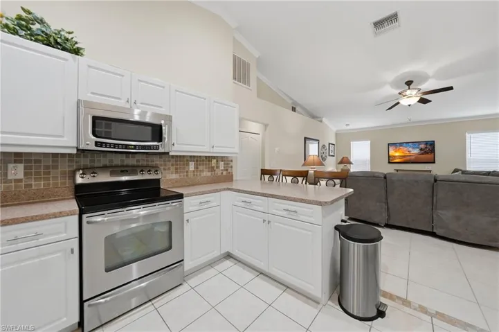 Kitchen with crown molding, stainless steel appliances, white cabinets, ceiling fan, and open floor plan