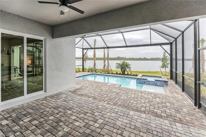 View of swimming pool with a ceiling fan, a patio area, a water view, and a pool with connected hot tub