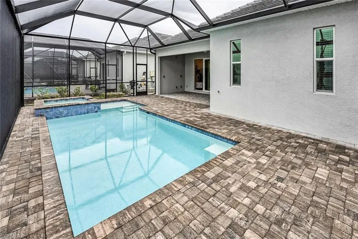 View of pool featuring glass enclosure, a pool with connected hot tub, and a patio area