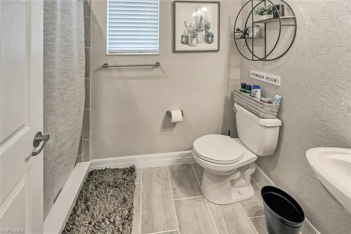 Full bath with a textured wall, toilet, wood tiled floor, a sink, and baseboards