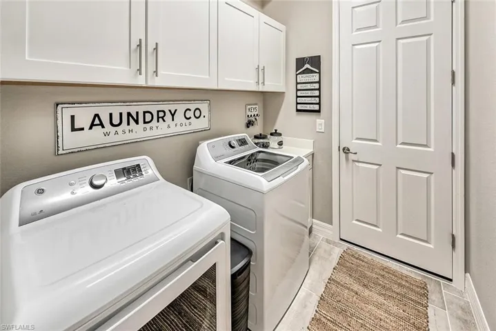 Clothes washing area with baseboards, cabinet space, and washer and dryer