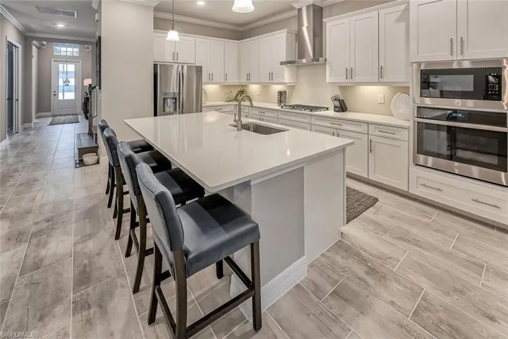 Kitchen featuring stainless steel appliances, a sink, white cabinets, light countertops, and wall chimney exhaust hood