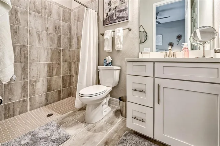 Full bath featuring toilet, a textured wall, a stall shower, and vanity